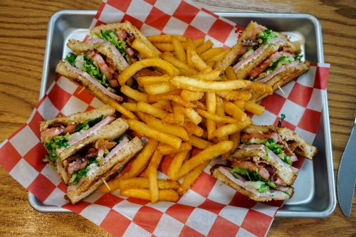 A tray with four sandwiches filled with lettuce, tomato, and meat, surrounded by golden French fries on a checkered paper.