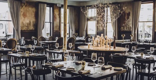 Elegant restaurant interior with dark wood tables, glassware, and a central candle display under soft lighting.
