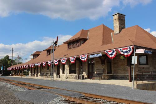 Historic train station with a stone facade, decorated with red, white, and blue bunting, alongside railway tracks.