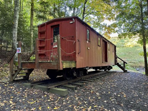 A red train caboose converted into a cabin, surrounded by trees and autumn foliage.