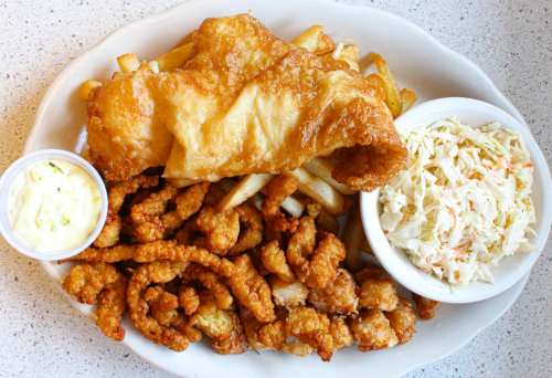 A plate of fried fish, crispy shrimp, French fries, and coleslaw served with a side of tartar sauce.