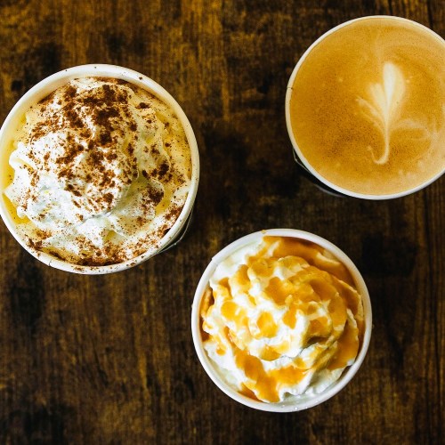 Three coffee drinks: one with whipped cream and chocolate, one with caramel, and a latte with a heart design.