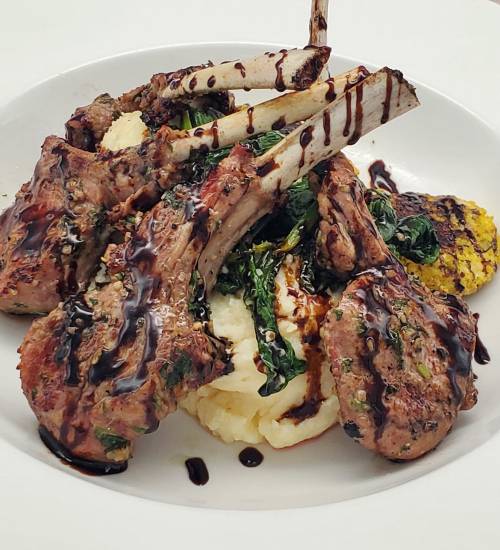 A plate of grilled lamb chops served with mashed potatoes, sautéed greens, and a drizzle of balsamic reduction.