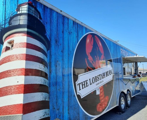 A food truck named "The Lobstah Buoy" featuring a lighthouse design and a large lobster graphic on a blue wooden background.