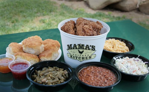 A bucket of fried chicken surrounded by biscuits, macaroni and cheese, coleslaw, green beans, and baked beans.