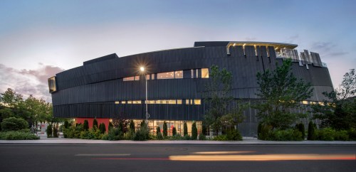 Modern building with a sleek, dark exterior, large windows, and landscaped surroundings at dusk.