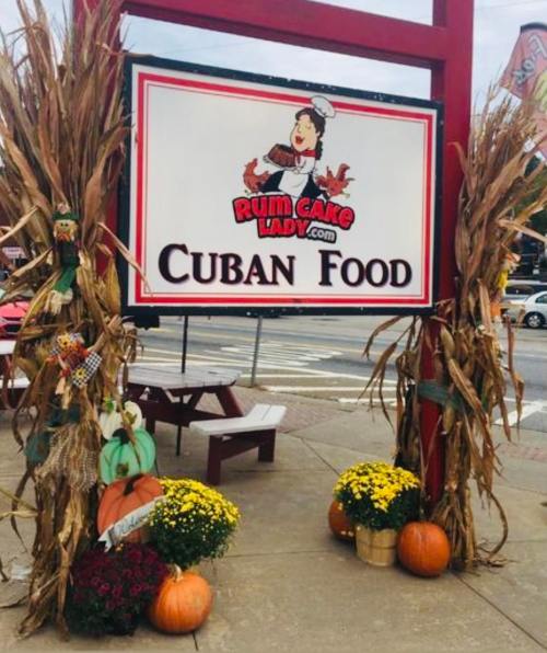 Sign for "Cuban Food" with decorative corn stalks, pumpkins, and flowers at Rum Cake Lady.