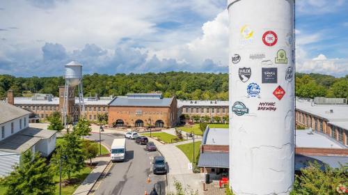 Aerial view of a building complex with a tall water tower featuring various stickers, surrounded by trees and vehicles.