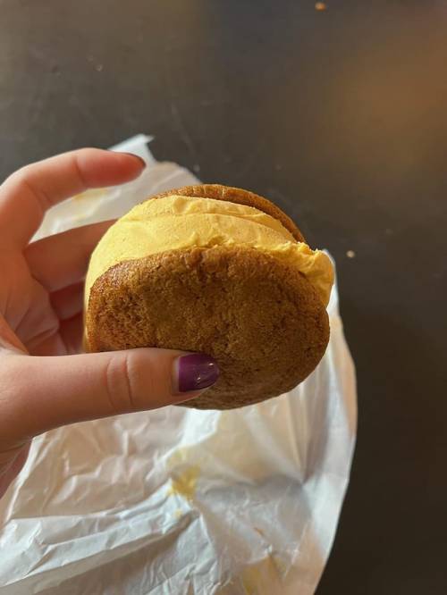 A hand holding a cookie sandwich filled with yellow cream, resting on a white wrapper.