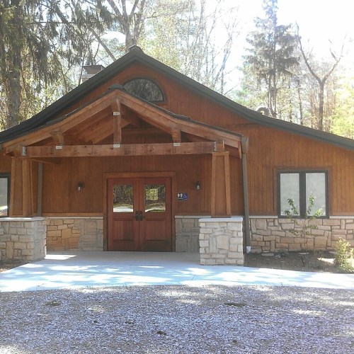 A wooden building with a stone foundation, featuring a large entrance and surrounded by trees.