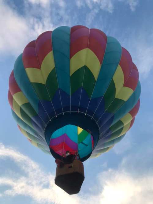 A colorful hot air balloon with a rainbow pattern floats against a blue sky with scattered clouds.