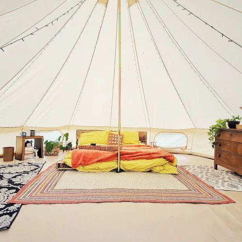 Cozy tent interior with a bed, colorful blankets, plants, and rugs, creating a warm, inviting atmosphere.