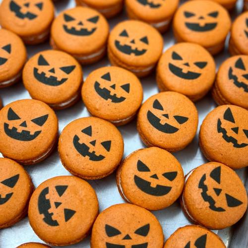 A close-up of orange macarons decorated with black jack-o'-lantern faces for Halloween.