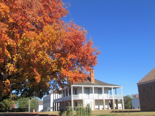 A historic building with a porch, surrounded by vibrant autumn foliage under a clear blue sky.