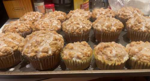 A tray of freshly baked muffins with a crumbly topping and a light glaze, varying in size.