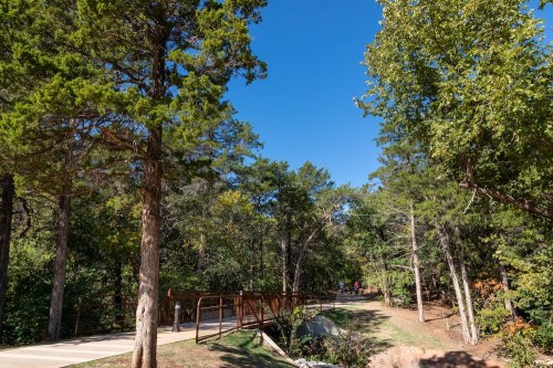A scenic pathway through a lush green forest under a clear blue sky, with trees lining the trail.
