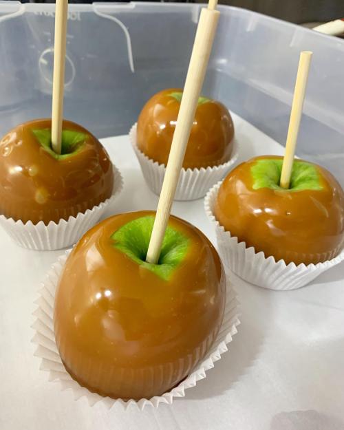 Four caramel apples with green centers on white cupcake liners, each with a wooden stick inserted.