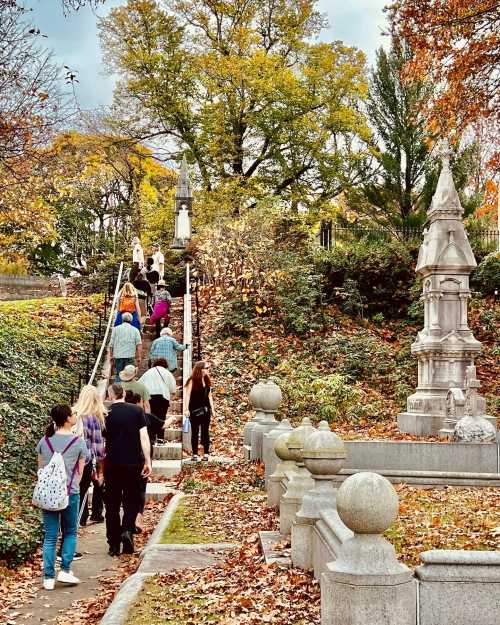 A group of people walking up stone steps surrounded by autumn foliage and decorative stone structures.