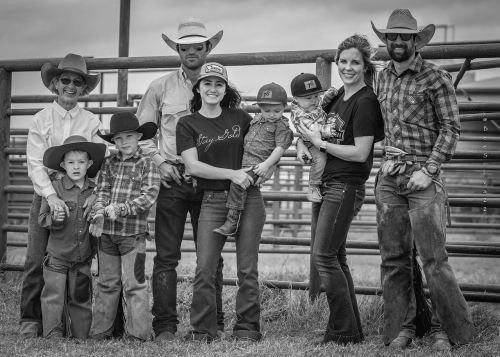 A black and white photo of a family in cowboy attire, posing together at a ranch with children and infants.