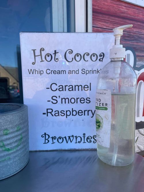 Sign listing hot cocoa toppings: caramel, s'mores, raspberry, with a hand sanitizer dispenser nearby.