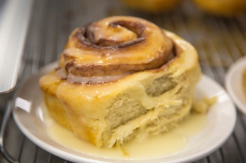 A close-up of a gooey cinnamon roll on a plate, drizzled with icing and resting on a cooling rack.