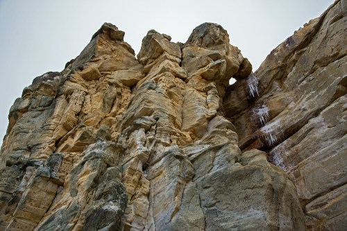A rugged rock formation with layered textures and a small waterfall cascading down the side.