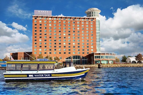 A water taxi in front of the Hyatt Regency hotel by the waterfront, with a blue sky and clouds above.