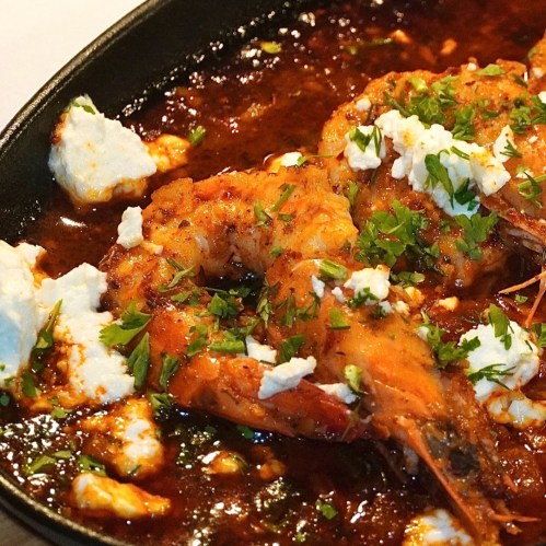 A close-up of shrimp in a spicy sauce, topped with crumbled cheese and fresh herbs, served in a skillet.