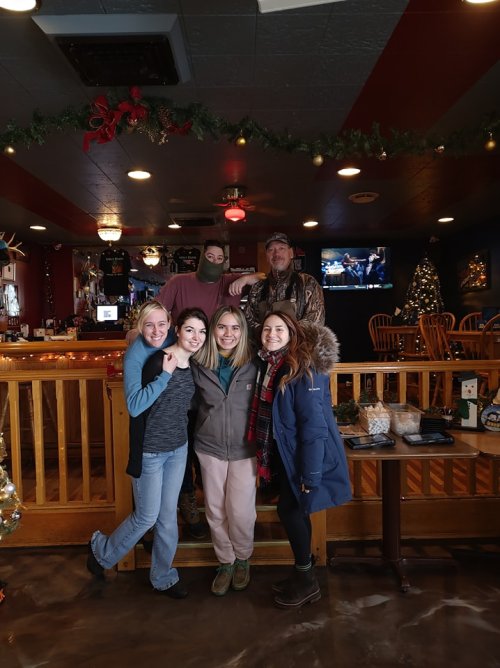A group of five people poses together in a festive bar decorated for the holidays.