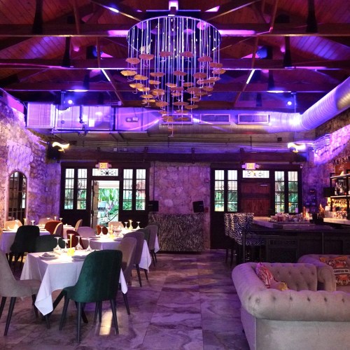 Elegant restaurant interior with stone walls, colorful lighting, and stylish furniture, featuring tables set for dining.