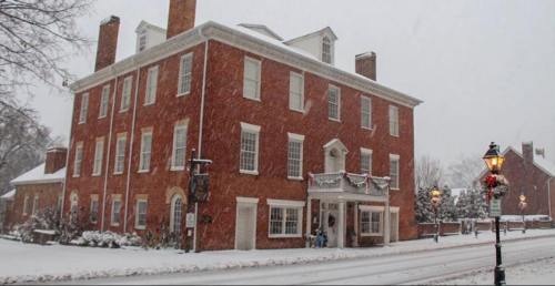 A historic red brick building covered in snow, with festive decorations and a lamppost in a winter scene.
