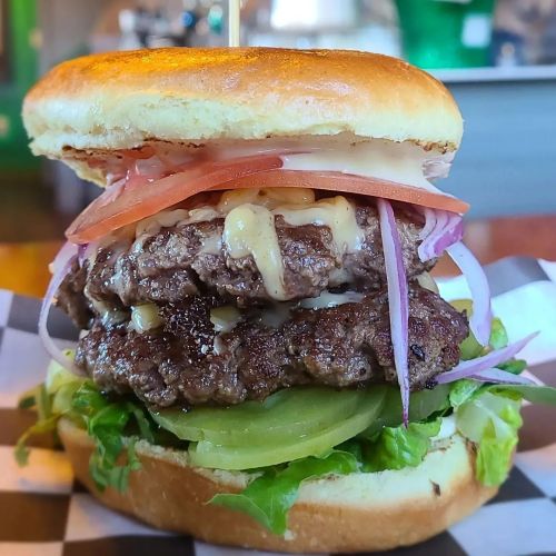 A stacked burger with two beef patties, lettuce, tomato, onion, and sauce on a toasted bun, served on a checkered plate.
