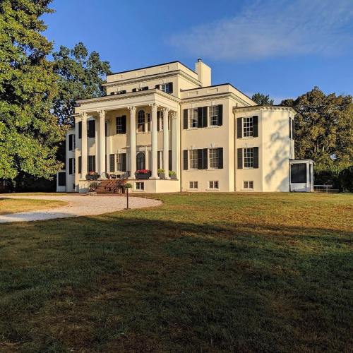 A large, elegant mansion with white columns, surrounded by trees and a grassy area under a clear blue sky.