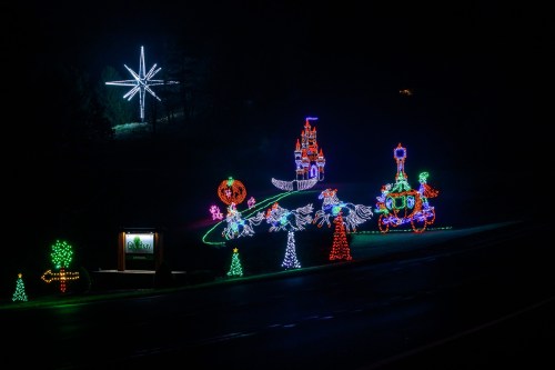Colorful holiday light display featuring a castle, train, and trees, illuminated against a dark night sky.
