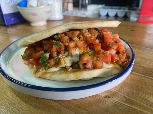A sandwich on a plate, filled with fresh tomato salsa and herbs, resting on a wooden table.