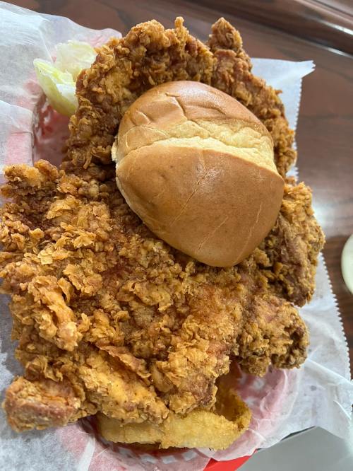 A large, crispy fried chicken breast placed on a bun, served in a basket with lettuce and paper lining.