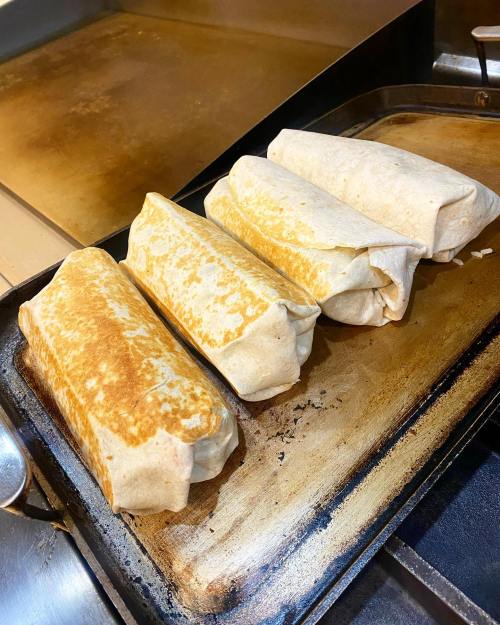 Four golden-brown burritos resting on a griddle, ready to be served.