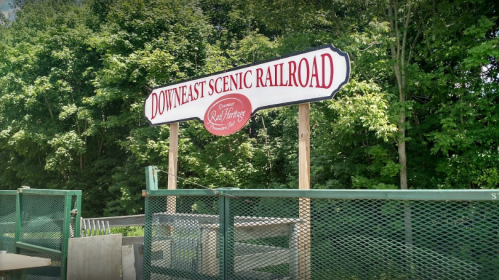 Sign for Downeast Scenic Railroad, surrounded by greenery, indicating a scenic train experience.