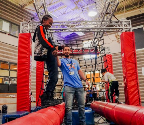 A child balances on a beam while an adult assists them in a fun indoor obstacle course.