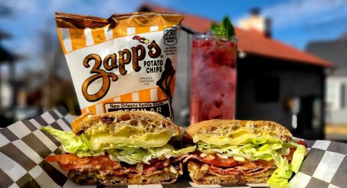 A delicious sandwich with lettuce, tomato, and bacon, served with Zapp's potato chips and a refreshing drink.