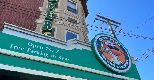 Sign for Duck Town Tavern & Liquors, open 24/7, with a green awning and a cartoon duck logo. Free parking in rear.
