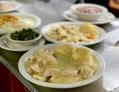A plate of chicken and dumplings in gravy, with sides of green beans and another dish in the background.