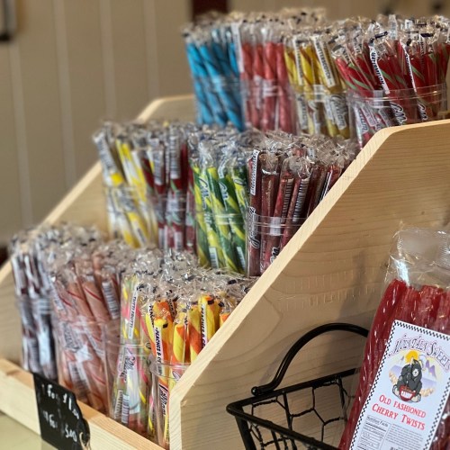 A wooden display filled with colorful, wrapped candy sticks in various flavors, including cherry twists.