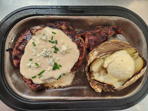 Grilled chicken with creamy sauce and blue cheese, served with a baked potato and sour cream on a metal tray.