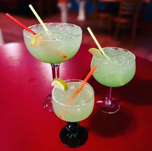 Three colorful cocktails with lime slices and straws on a red table.