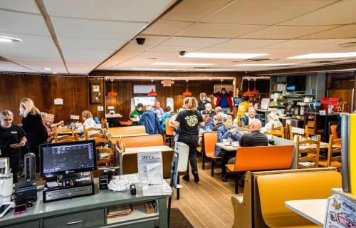 A busy diner with patrons seated at tables, a server attending to customers, and a warm, inviting atmosphere.