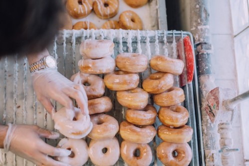 A person in gloves arranges freshly glazed donuts on a cooling rack.