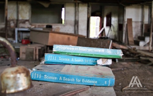 Three old, worn textbooks titled "Progress in Mathematics" and "Science: A Search for Evidence" on a dusty surface in an abandoned room.