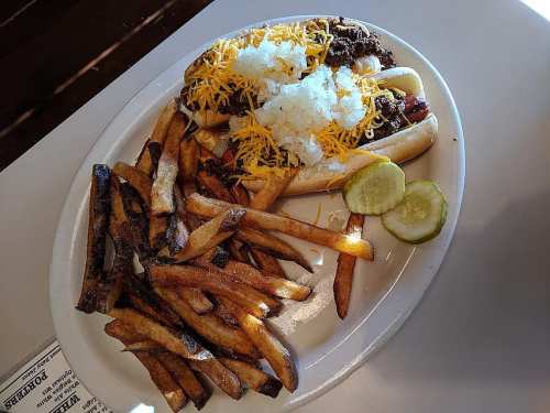 A plate of two loaded hot dogs topped with cheese and onions, served with a side of crispy French fries and lime wedges.