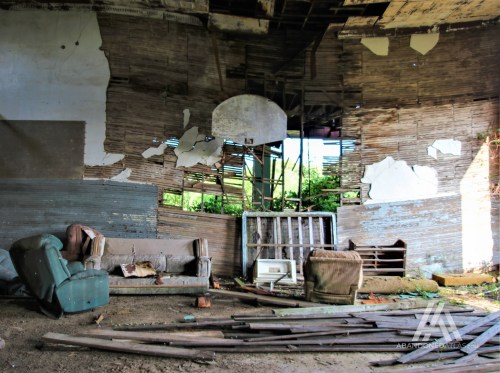 Abandoned interior of a dilapidated building with worn furniture and peeling walls, surrounded by debris.